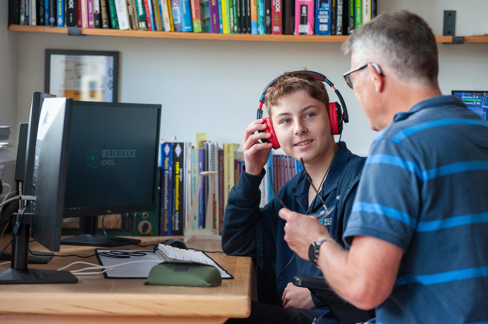 A teacher supervises a pupil wearing headphones