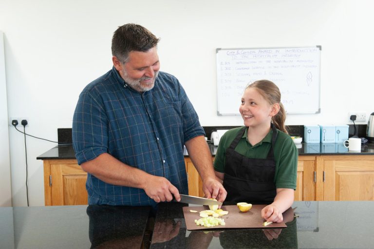 A pupils smiles at a teacher chopping an apple