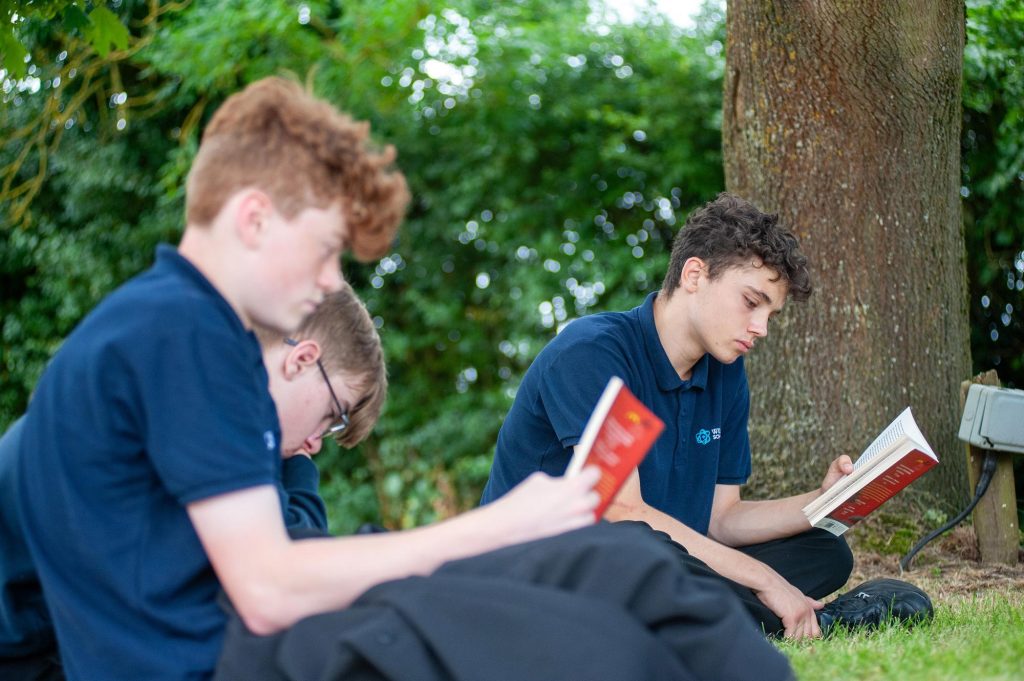 Three pupils read a book under a tree