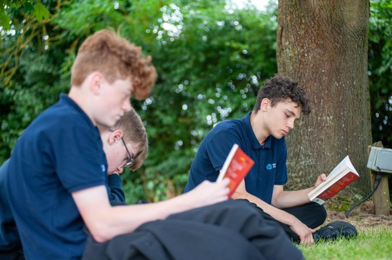 Three pupils read a book under a tree