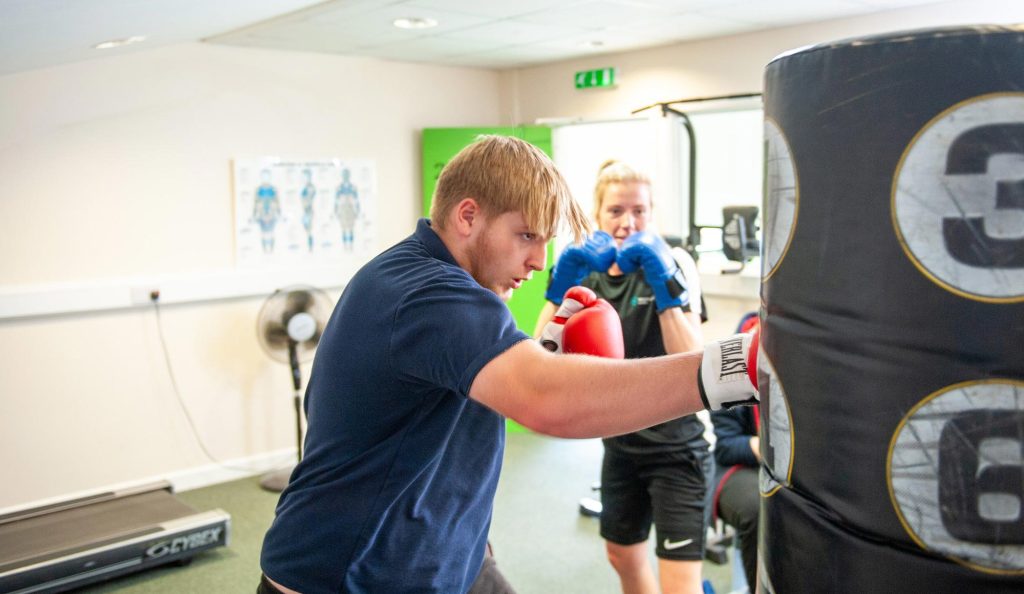 A pupil boxes with a punchbag, watched on by a trainer