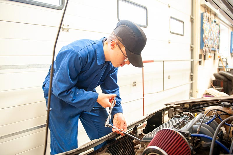 A teenage mechanic works on a car engine